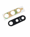 Two replacement lens protectors for a smartphone camera lens: one black silicone protector with white printed alignment markings, and one clear protective film with a brown adhesive backing and green tape remnants, shown on a plain white background.