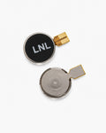 Two small round replacement battery components on a clean white background, one with a black face printed with 'LNL' in white and the other showing the metallic internal cell, both with gold-colored connector tabs.
